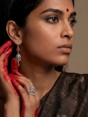 Model in a dark saree with mehendi-dyed hands, wearing a silver earring and ring