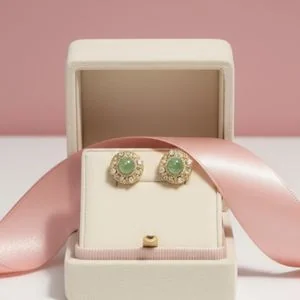 Pair of green gemstone studs in an ivory box with a pink ribbon
