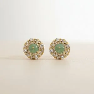 Pair of green cabochon studs with a white-stone halo on a pale surface, close detail