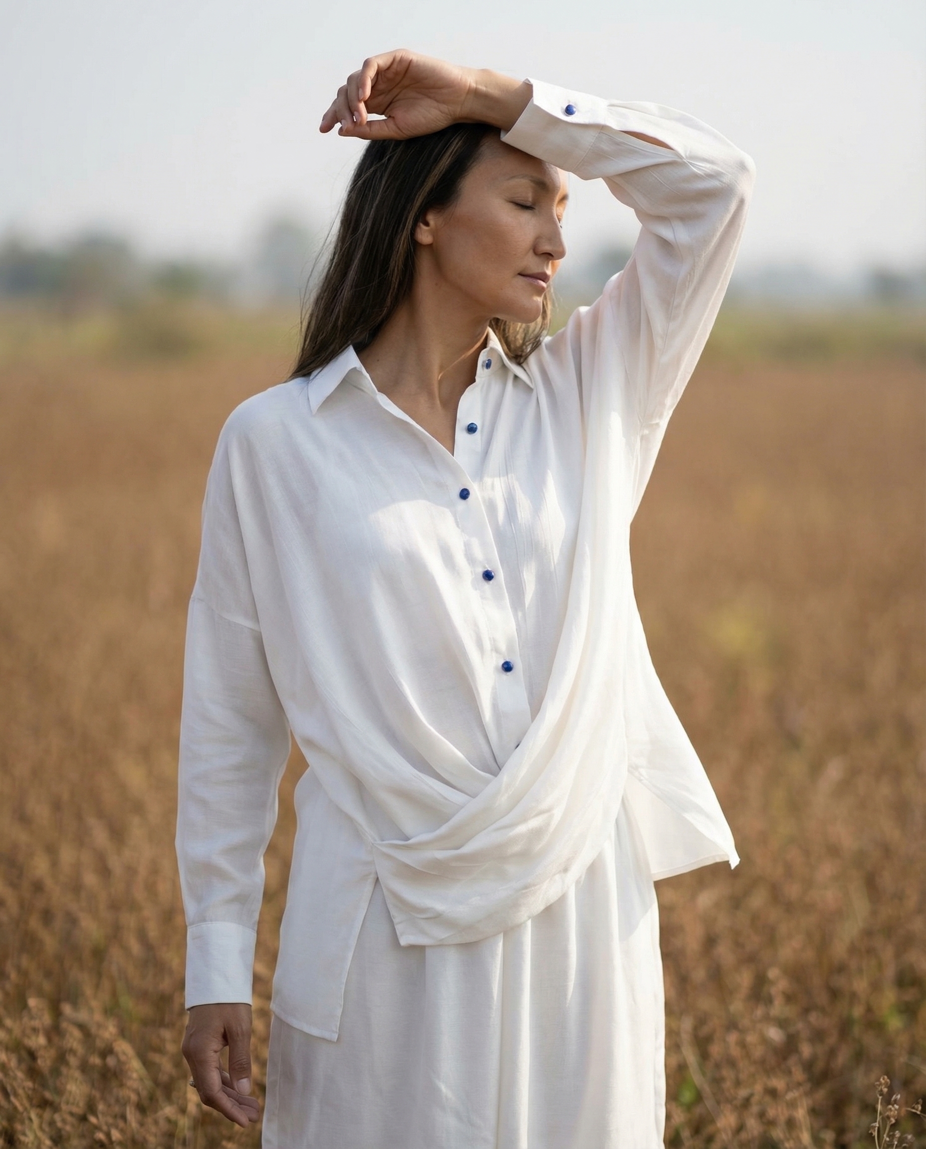 The K Way model in a flowing white gemstone-button outfit standing in a field