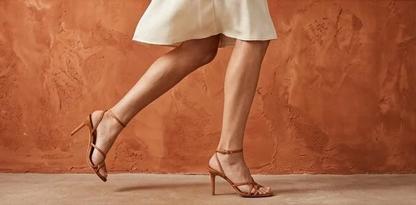 Footwear look on a model in strappy heels, mid-step past a terracotta wall, an AI photoshoot by Kaptured.AI